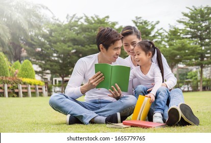 Portrait Of Happy Asian Family Man Woman And Little Girl Reading Outside. Asian Family Of Three Have Fun Reading Book Together Outdoor.  Home School Education Family Lifestyle Spring Or Summer Concept