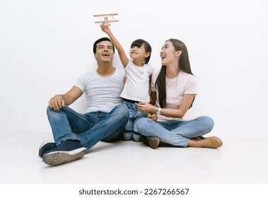 Portrait of Happy Asian family sitting on the floor laughing and playing with toy airplane together isolated on white wall background. Asia Family relaxing enjoying cozy leisure lifestyle concept.