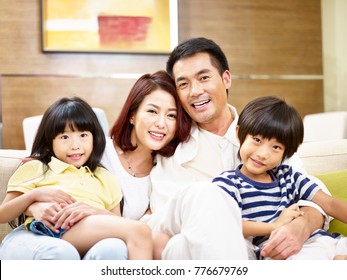 Portrait Of A Happy Asian Family Sitting On Couch At Home Looking At Camera Smiling.