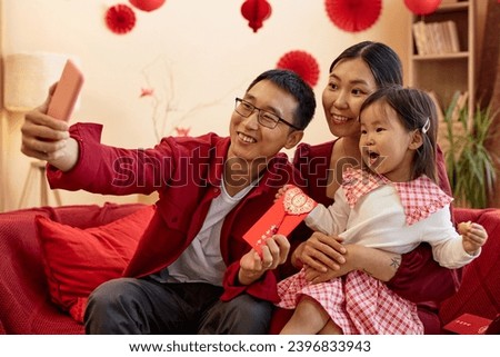 Portrait of happy Asian family taking selfie photo together and wearing red on Chinese New year Translation Have overflowing abundance hundred years
