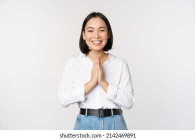 Portrait of happy asian girl laughing and smiling, showing thank you, namaste gesture, grateful for smth, standing over white background