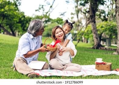 Portrait of happy asian grandfather with grandmother and asian little cute girl enjoy relax in summer park.Young girl with their laughing grandparents smiling together.Family and togetherness