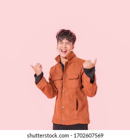 Portrait of happy asian handsome young man in fashionable clothing with standing thumbs up and smiling isolated on pink background.