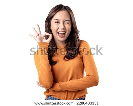 A portrait of a happy Asian Indonesian woman wearing an orange sweater and displaying the OK hand sign, isolated on a white background
