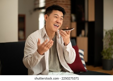 Portrait of happy asian man holding cellphone near mouth and recording message, using mobile voice recognition or digital assistance app speaking with virtual assistant - Powered by Shutterstock