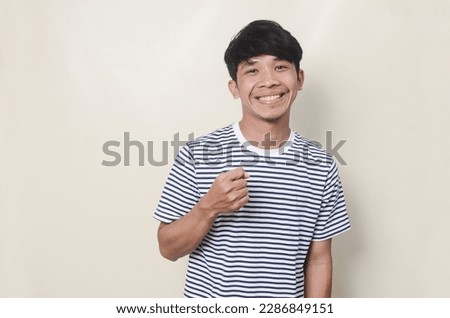 Portrait of happy Asian man pointing in striped t-shirt on isolated background.