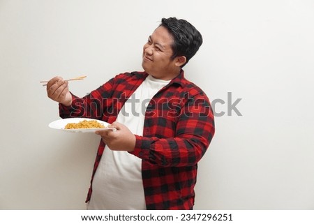 Portrait of Happy Asian man in red plaid shirt eating delicious instant noodles with chopsticks served on plate. . Eating lunch concept. Isolated on white background