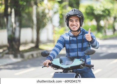 Portrait Of Happy Asian Man Riding On Motorbike In City Street And Showing Thumb Up