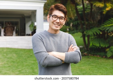 Portrait Of Happy Asian Man Wearing Glasses Smiling In Garden Outside Family Home. Enjoying Leisure Time Alone At Home.