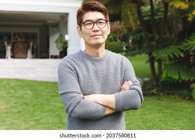 Portrait Of Happy Asian Man Wearing Glasses Smiling In Garden Outside Family Home. Enjoying Leisure Time Alone At Home.