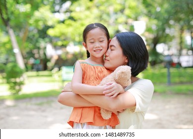 Portrait Of Happy Asian Mother Cuddle Daughter And Hugging Teddy Bear Doll In The Garden. Mom And Child Girl With Love And Relationship Concept.