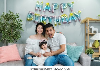 Portrait Of A Happy Asian Nuclear Family Looking At Camera While Having Birthday Celebration In A Decorated Living Room At Home