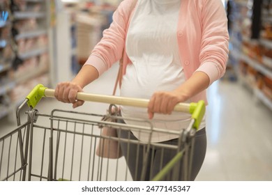 A portrait of happy Asian pregnant woman customer walking along supermarket, buying items on grocery products shelves with basket. Food shopping. Having a baby. Family people lifestyle. Mom. - Powered by Shutterstock