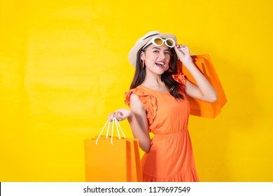 Portrait Of A Happy Asian Pretty Girl Holding Shopping Orange Bags Away Isolated Over Yellow Background,colorful Shopping Concept.
