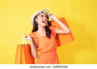 Portrait Of A Happy Asian Pretty Girl Holding Shopping Orange Bags Away Isolated Over Yellow Background,colorful Shopping Concept.