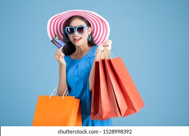 Portrait Of A Happy Asian Pretty Girl Holding Shopping Bags While Hold Credit Cards Looking Away Isolated Over Blue Background,colorful Shopping Concept.