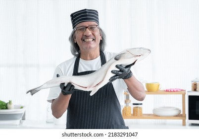 Portrait of happy Asian senior man chef is holding and showing fresh whole salmon in his hands smiling at camera and standing in kitchen. Elderly chef prepare fish for ingredient in japanese food - Powered by Shutterstock