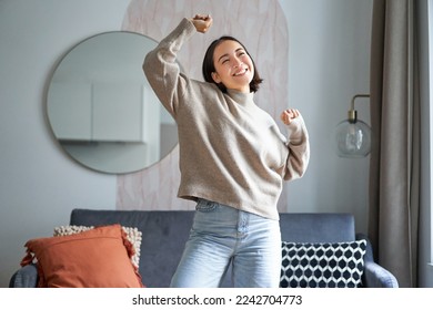 Portrait of happy asian woman dancing, rejoicing and triumphing, feeling upbeat at home. Copy space - Powered by Shutterstock