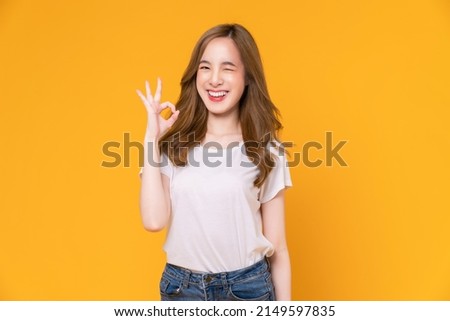 Portrait happy Asian woman shows ok sign and looking at the camera on yellow background.