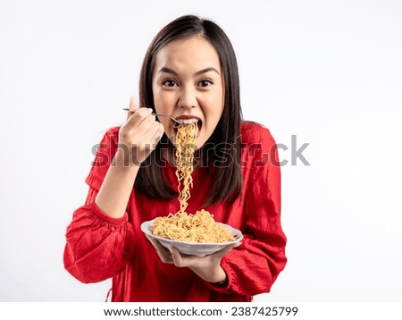 A portrait of a happy Asian woman wearing a red shirt, eating noodles. Isolated against a white background.