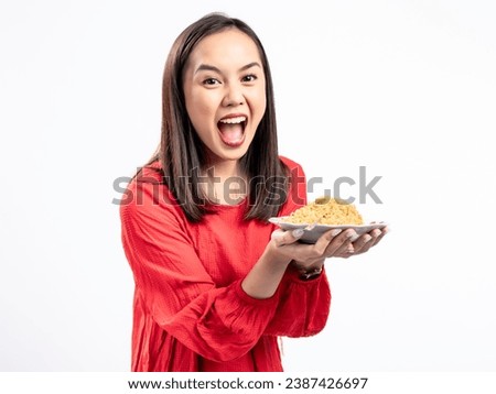 A portrait of a happy Asian woman wearing a red shirt,  presenting noodles, and about to eat them. Isolated against a white background.
