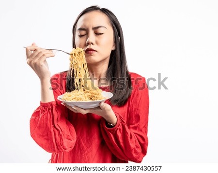 A portrait of a happy Asian woman wearing a red shirt, posing eating noodles. Isolated against a white background.