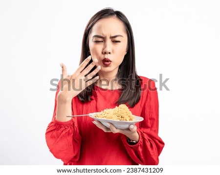 A portrait of a happy Asian woman wearing a red shirt, eating noodles, and feeling a bit spicy. Isolated against a white background.
