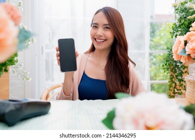 Portrait Of A Happy Asian Young Adult Florist Floral Shop With Cheerful Smiling Hand Show Smartphone Small Business Owner,Florist Showing A Smartphone While Surrounded With Flowers And Plants 