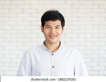 Portrait Of A Happy Asian Young Businessman On White Brick Wall Background  Looking At Camera With A Warm Smile And Self-confident. Close Up Face Of Happy Successful Business Man.