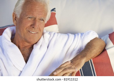 Portrait Of A Happy Attractive Handsome Senior Man In A White Bathrobe Sitting Down Outside Smiling.