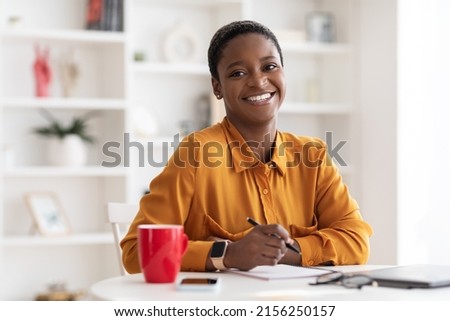Portrait of happy attractive short-haired millennial black lady in casual outfit working at white cozy office, taking notes, copy space. Millennials lifestyles, job opportunities for young people