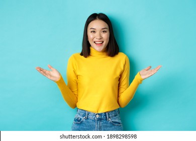 Portrait Of Happy Attractive Woman Spread Hands Sideways And Smiling, Surprised To See You, Standing Over Blue Background