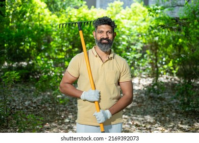 Portrait Of Happy Beard Indian Man Volunteer Holding Cleaning Equipments To Clean Fallen Leaves In The Forest Or Nature, Spring Trash Cleaning In Park. Looking At Camera.