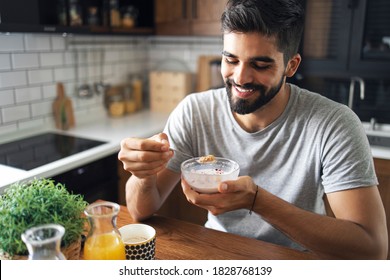 Portrait of happy bearded fit man sitting at kitchen table, eating cereals for breakfast - Powered by Shutterstock