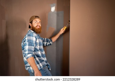 Portrait Of Happy Bearded Painter In Cap Painting A Wall With Paint Roller. House Painter Concept