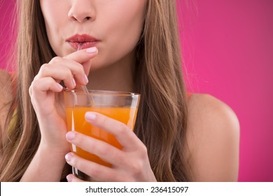 Portrait of happy beautiful brown haired girl drinking orange or carrot juice on rose background smiling looking at camera  close up 