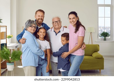 Portrait of a happy beautiful extended multi generational family all together at home. Cheerful, joyful children, parents and grandparents standing in the living room, hugging and smiling - Powered by Shutterstock