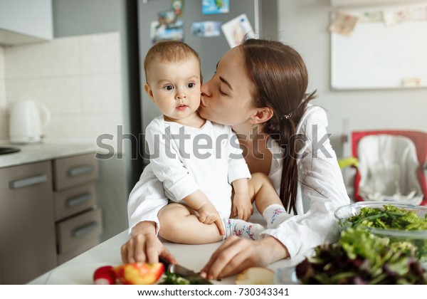 Portrait of happy beautiful mother kissing her lovely baby in cheek in