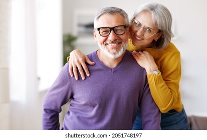 Portrait of happy beautiful senior caucasian family couple in love smiling at camera, retired man and woman hugging embracing while relaxing on sofa in living room at home, enjoying life on retirement - Powered by Shutterstock