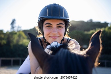 Portrait of a happy beautiful white woman in her competition uniform riding her bay horse on a dressage ring with a forest in the background on a sunny day - Powered by Shutterstock