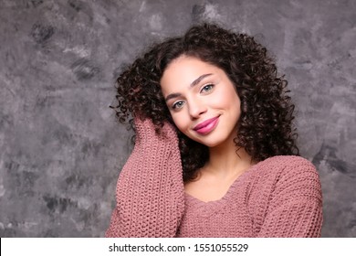 Portrait of happy beautiful woman with long bouncy curles hairstyle and professional make up on, posing over grunged stone background. Fashion shot of young gorgeous female. Close up, copy space.