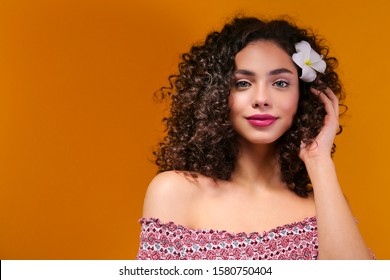 Portrait of happy beautiful woman with long bouncy curles hairstyle and professional make up on, posing over isolated yellow background. Fashion shot of young gorgeous female. Close up, copy space.