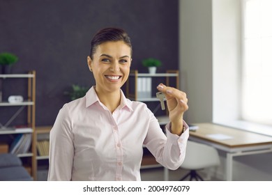 Portrait Of Happy Beautiful Young Realtor, Real Estate Agent, Mortgage Broker, Corporate Manager Or Tenant Standing In Office, Holding Keys To New Flat Or House, Smiling And Looking At Camera