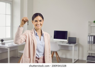 Portrait Of Happy Beautiful Young Woman In Suit Standing In Office And Holding Keys. Smiling Realtor, Real Estate Agent, Mortgage Broker, Corporate Manager Or Tenant Showing Keys To New Flat Or House