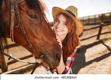 Portrait of happy beautiful young woman cowgirl in hat with her horse on ranch