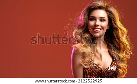 Portrait of happy beautiful young woman with bright shiny makeup. Smiling Blonde with brightly colored long hair. Pretty girl with long curly hair.  Fashion model in a shiny dress posing at studio.