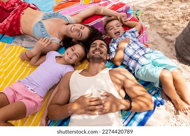 Portrait of happy biracial family lying on towel at beach. Spending quality time, lifestyle, family, summertime and vacation concept. - Powered by Shutterstock