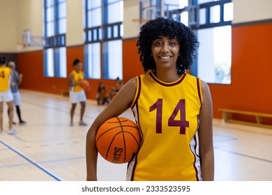 Portrait of happy biracial female basketball players holding and playing basketball at gym. Sport, activity, togetherness and lifestyle, unaltered. - Powered by Shutterstock