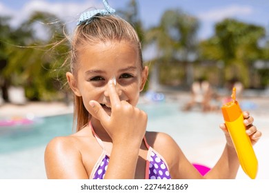 Portrait of happy biracial girl smiling and applying sunscreen by the swimming pool. Spending quality time, lifestyle, childhood, summertime and vacation concept. - Powered by Shutterstock