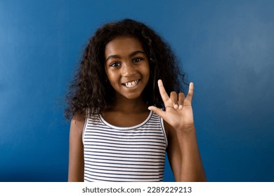 Portrait of happy biracial girl using sign language with hand on blue background. Childhood, learning, disability, inclusivity and communication. - Powered by Shutterstock